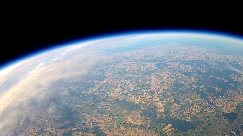 Erdkrümmung mit Feldern, Wäldern und einem Fluss unter dünner blauer Atmosphäre