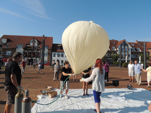Mehrere Personen halten den Hals eines großen weißen Wetterballons, davor liegen Gasflaschen
